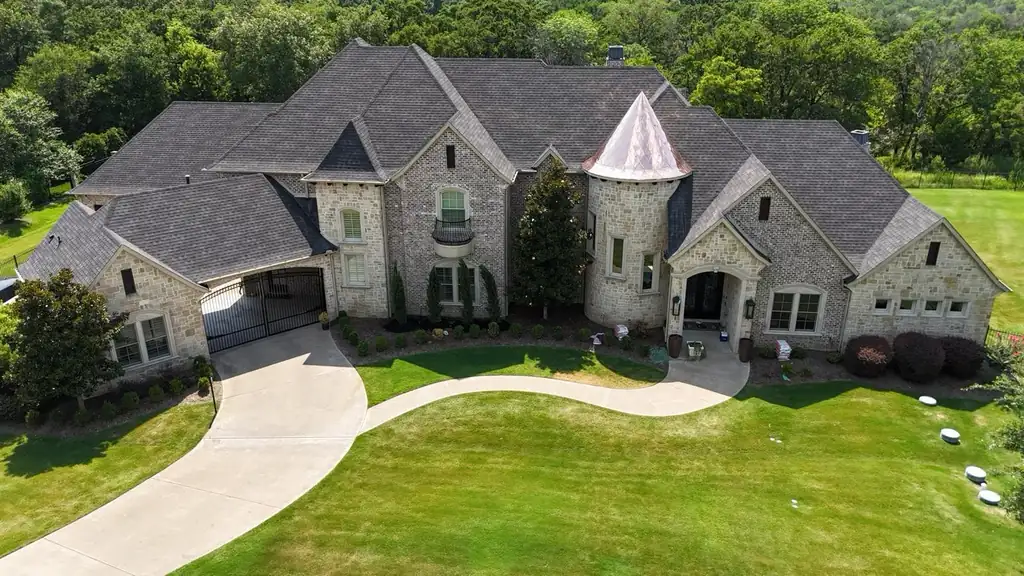 Aerial view of a stone and brick home with a dark shingle roof and a copper turret cap